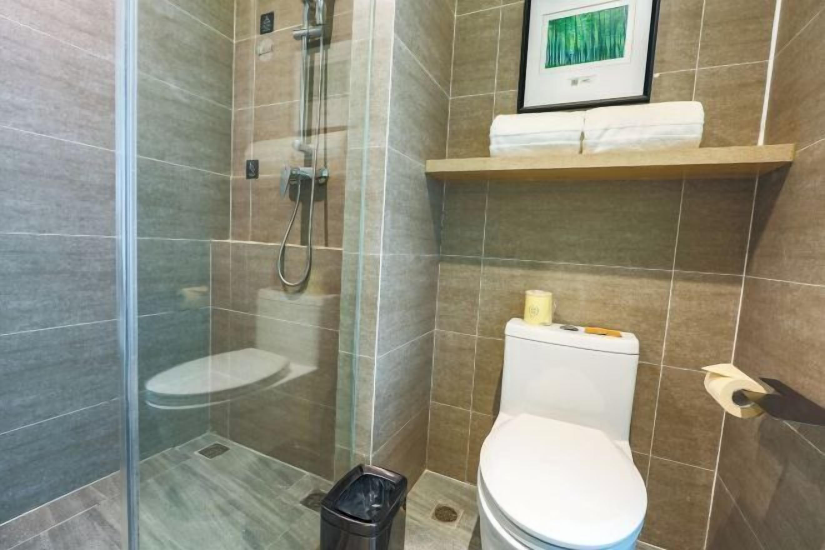 A bathroom with a glass-enclosed shower, a toilet, and a shelf with a towel.