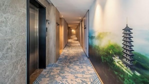 Un couloir d’hôtel avec un tapis à motifs, des murs en marbre et une fresque représentant une pagode.