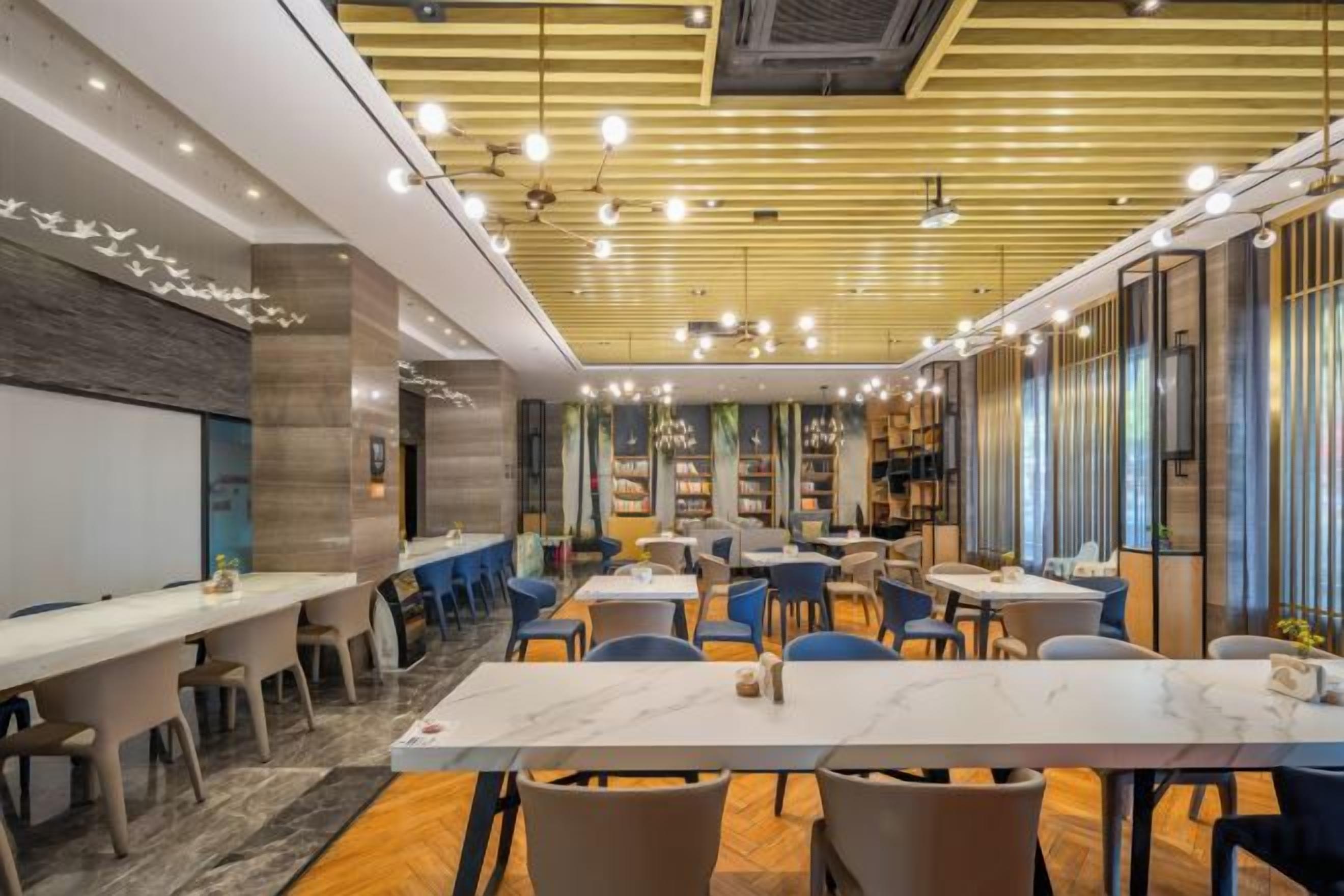 Un restaurant doté de nombreuses tables et chaises, d’un design moderne au niveau du plafond et d’un espace bar.