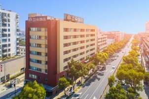 Un hotel de varios pisos con diseño moderno, que destaca por su fachada en rojo y beige, situado a lo largo de una calle arbolada.