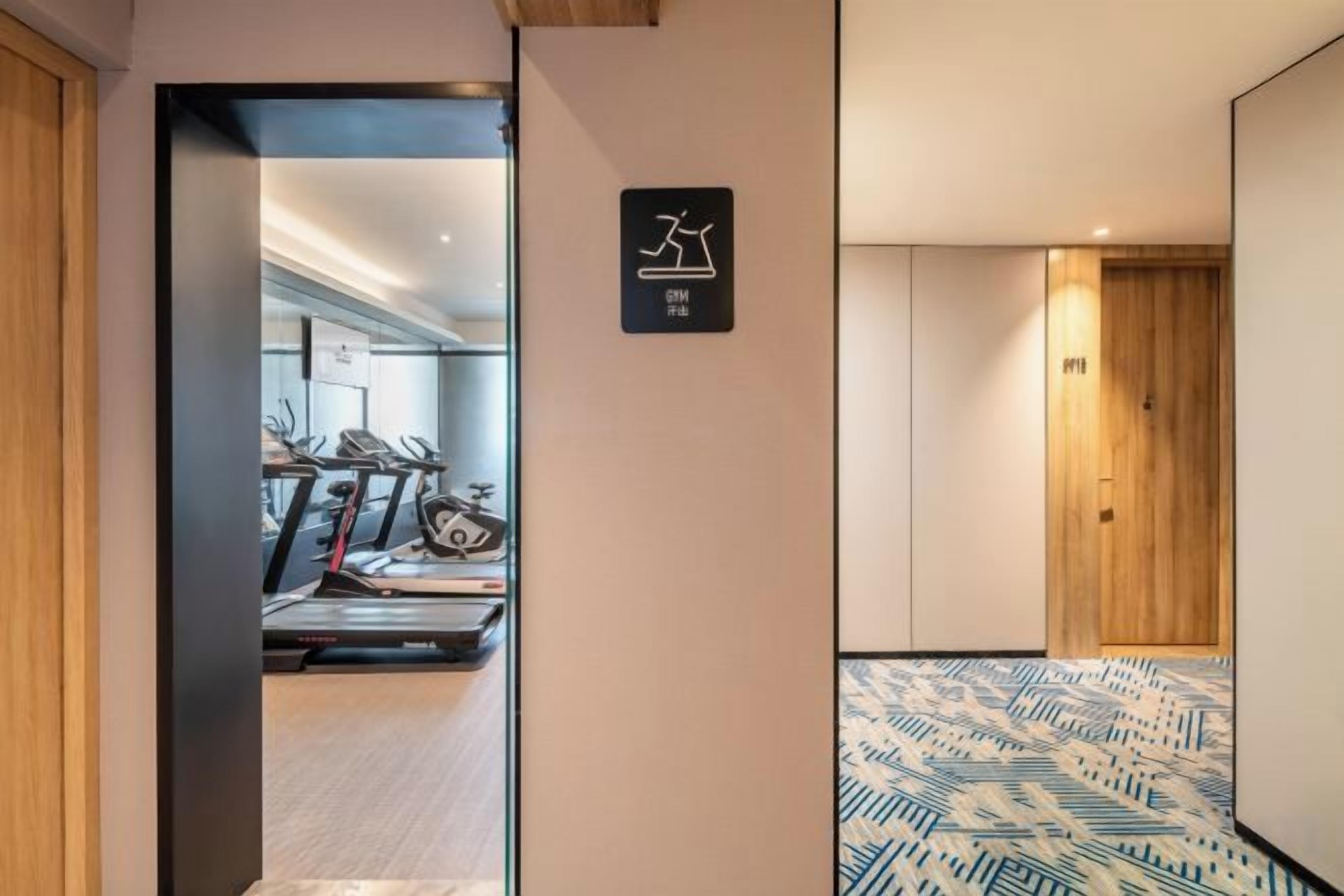 A hallway leading to a gym area with exercise equipment, a wooden door, and patterned flooring.