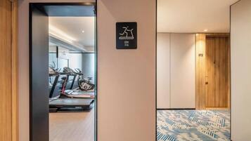A hallway leading to a gym area with exercise equipment, a wooden door, and patterned flooring.