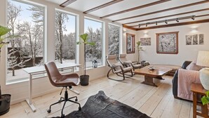 Amplia habitación con ventanas grandes, techo de madera, una mesa de comedor y muebles modernos.