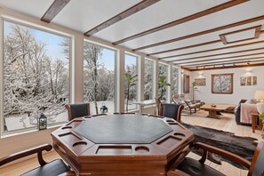 A spacious room with a large octagonal table, multiple chairs, and large windows offering a view of snow-covered trees.