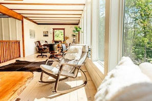A cozy room with a rocking chair, wooden flooring, and a large window offering a view of trees.