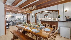 Un comedor con una mesa de madera dispuesta para seis, una cocina con armarios blancos y una sala de estar con sofá y mesa de centro.