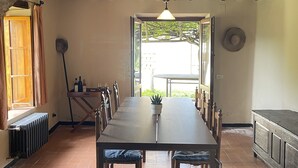 Ein Essbereich mit einem langen Holztisch, Stühlen, einem Heizkörper, einer Topfpflanze und einem Hut an der Wand.