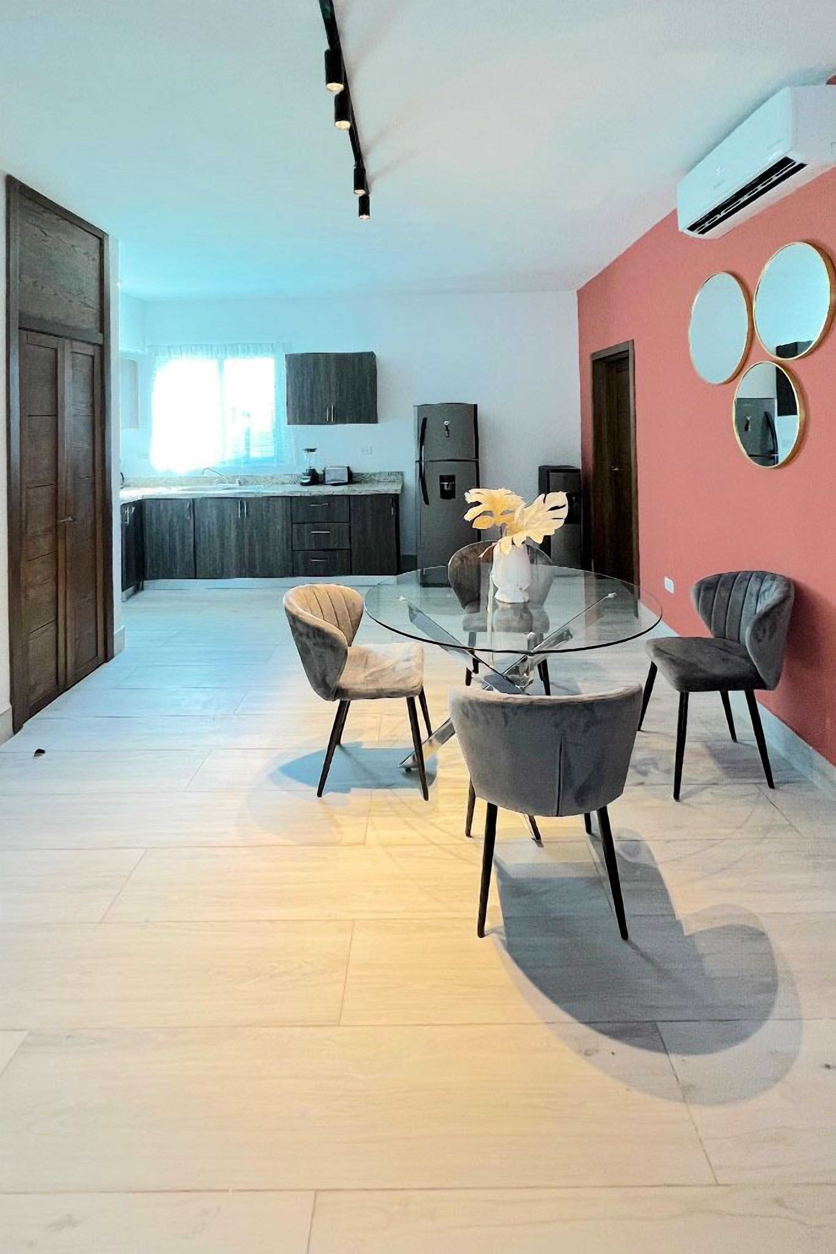 Una cocina moderna con armarios oscuros, una mesa de comedor de vidrio y una pared de acento roja.