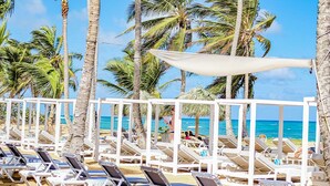 A beachside lounge area with white sunbeds and a white canopy, surrounded by palm trees and the ocean. - Playa Palmera Beach Resort  (Punta Cana)