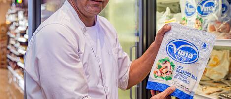 A person in a white chef's uniform holding a bag of seafood mix.