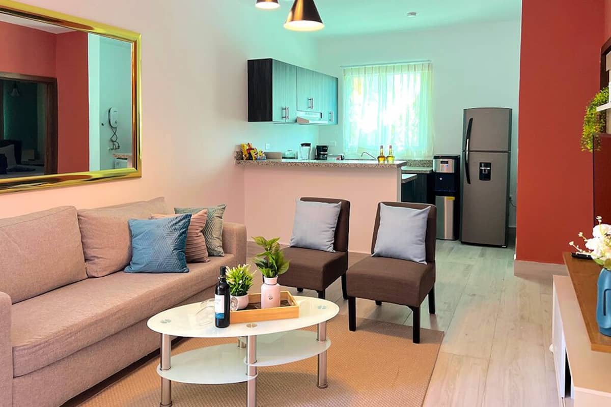A modern living room with a sofa, two armchairs, a coffee table, and a kitchen in the background.