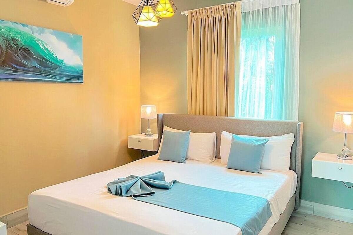 A hotel room with a bed, two bedside tables with lamps, a painting on the wall, and a window with curtains.