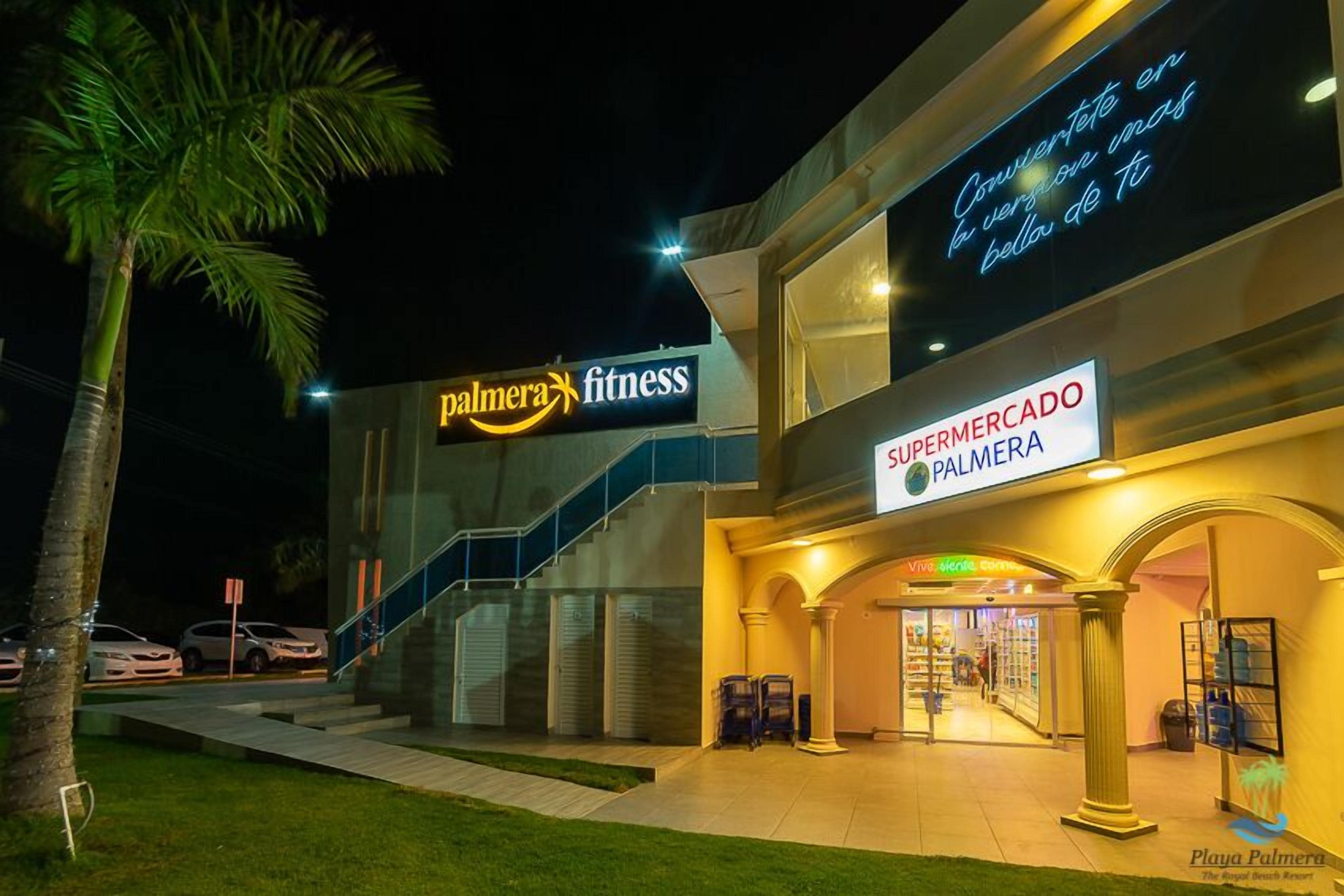 Un edificio commerciale a più livelli con un cartello 'Palmera Fitness', un cartello 'Supermercado Palmera' e un cartello 'Playa Palmera'.