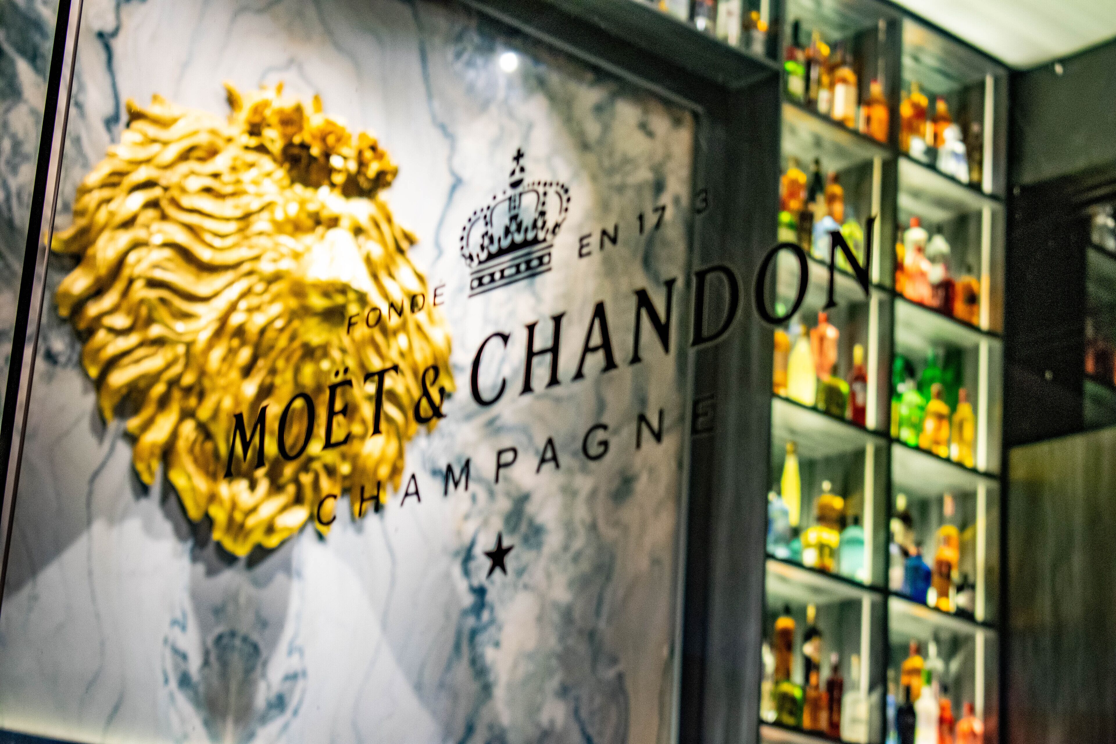 Et skilt fra Moët & Chandon med et løve-emblem, omgivet af hylder med forskellige spiritusflasker.