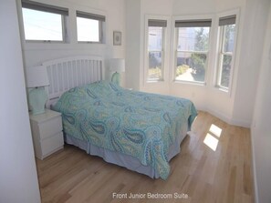 Relax in this cozy bedroom with a comfortable bed, a nightstand, and a lamp, offering a view of the outdoors through three windows.