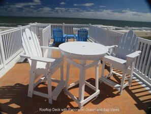 Relax and dine on the rooftop deck with ocean and bay views, featuring a table and Adirondack chairs.