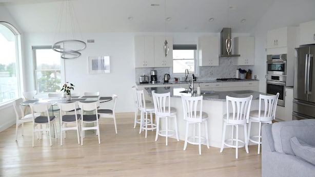 A modern kitchen with white cabinetry, a central island, and a dining area with white chairs.