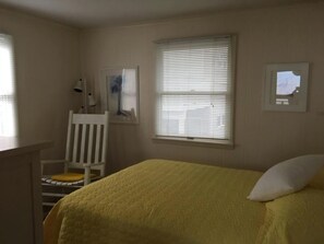 A bedroom with a bed, a chair, a window with blinds, and a wall-mounted picture.