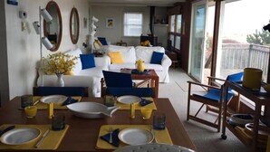 A dining area with a table set for four, a white sofa, and a large window with a view. - Sought after LEYC oceanfront (Beach Haven)