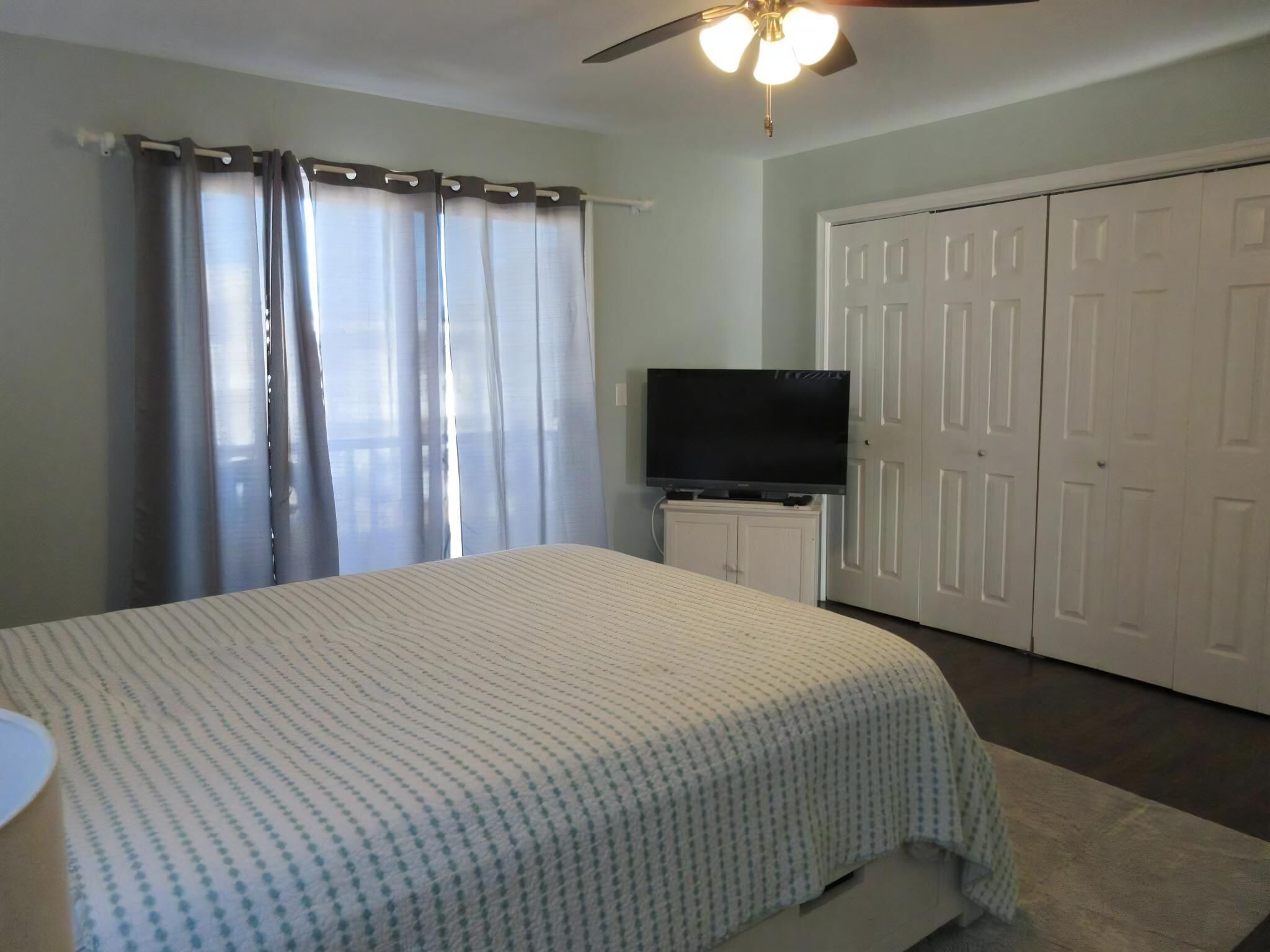 A bedroom with a bed, a TV, a ceiling fan, and a wardrobe.