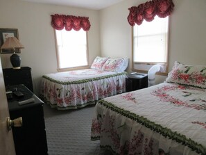 Two single beds with floral-patterned bedding, each flanked by a nightstand, are positioned in this classic hotel room.