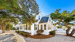 Une maison blanche avec un toit à pignon, entourée de gravier et d’arbres.