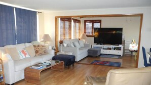Ein Wohnzimmer mit Sofa, Sessel, Couchtisch, Fernseher und einem Essbereich mit Tisch und Stühlen.
