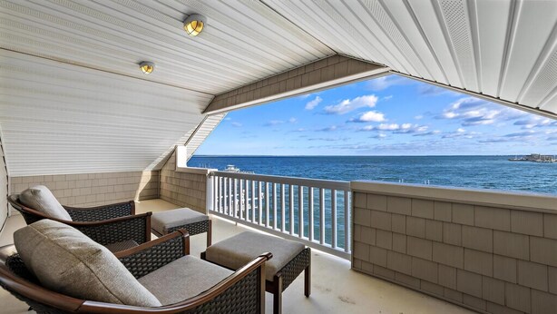Un balcon doté de meubles en osier, une vue sur la mer et un plafond blanc avec des spots encastrés.