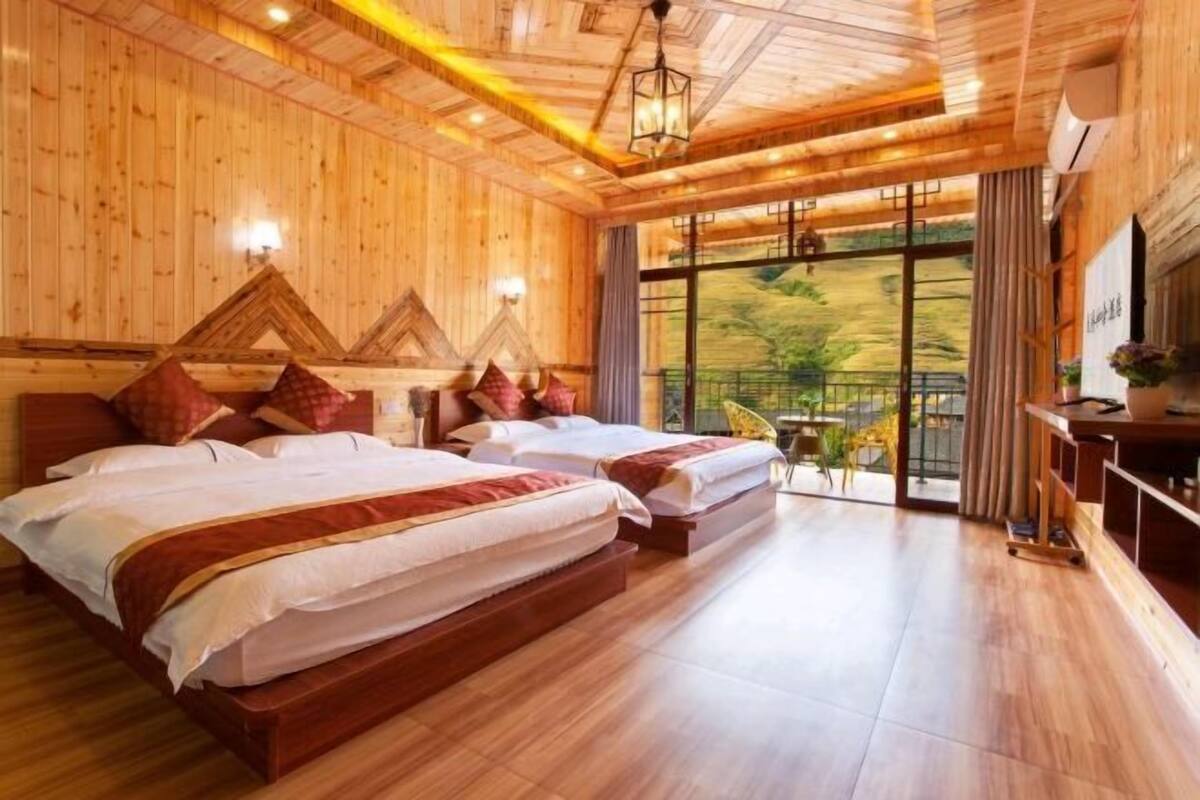 A wooden-themed hotel room with two beds, a TV, and a view of the outdoors.