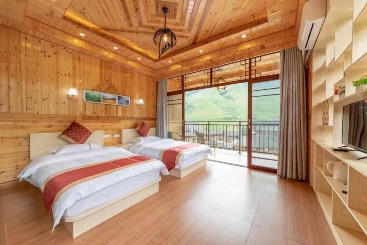 A wooden cabin-style bedroom with two beds, a large window, and a balcony.