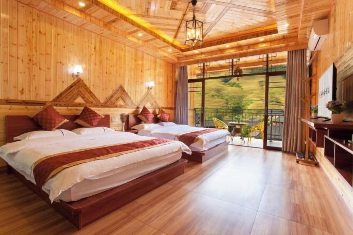 A wooden-themed hotel room with two beds, a desk, and a large window with a view.