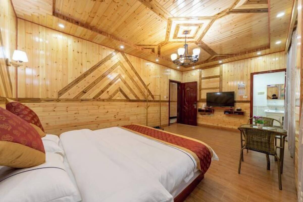A wooden-paneled room with a bed, a television, and a wicker chair.