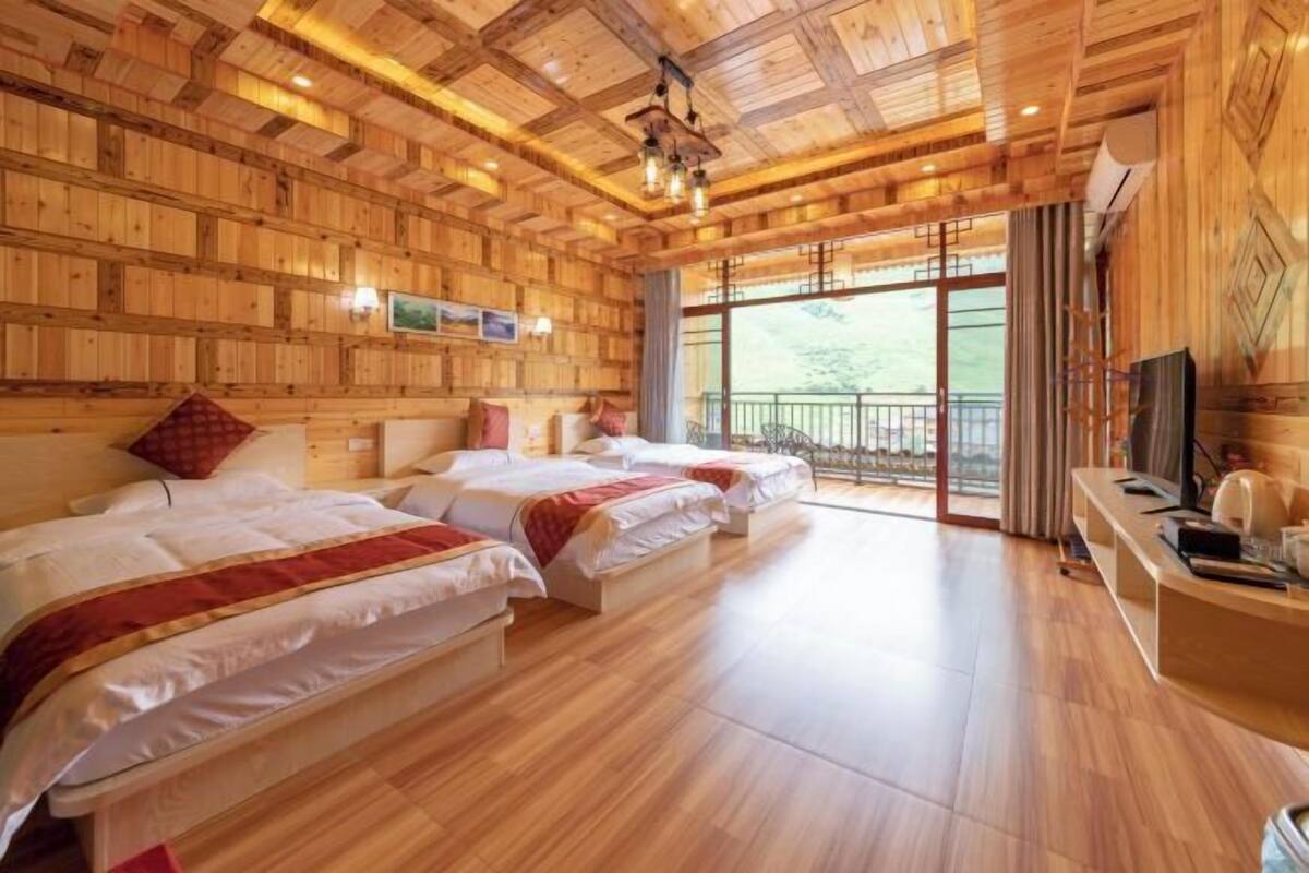 A room with wooden walls and floors, two beds with white bedding, a TV, and a balcony with a view.