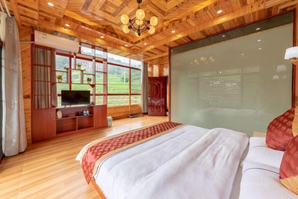A spacious bedroom with a large bed, wooden ceiling, and a television on a wooden cabinet.