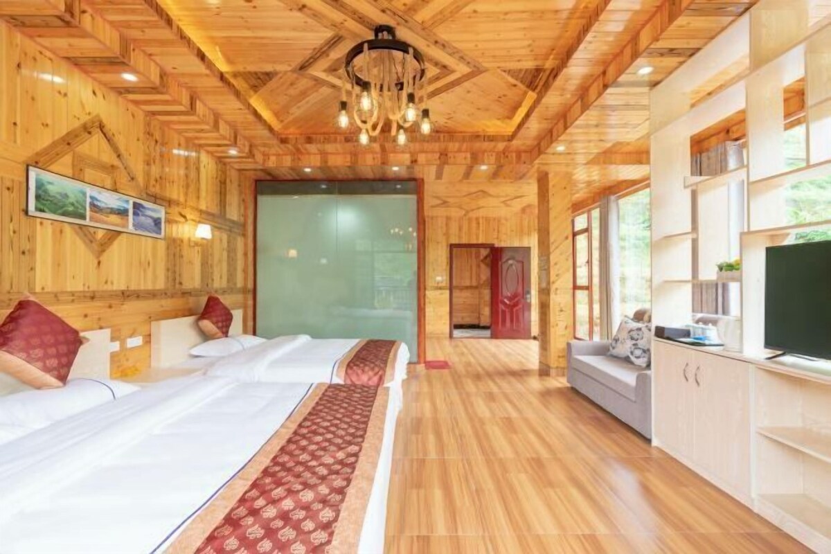 A wooden cabin-style room with a bed, a sofa, a TV, and a large window.