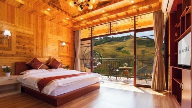 A wooden interior bedroom with a bed, a small table, and a view of a green landscape through a glass door. - Longji Rice Terraces Heshe Homestay (Longsheng)