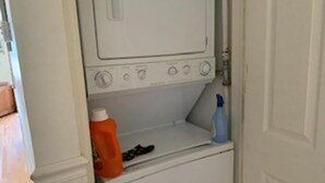 Une machine à laver blanche, avec une bouteille de lessive et un flacon pulvérisateur bleu posés sur le dessus.