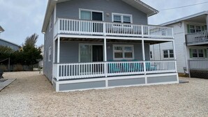 A two-story building with a balcony on the second floor, a covered porch on the first floor, and a gravel driveway. - Newly renovated duplex located on the ocean block in the heart of Surf City. (Surf City)