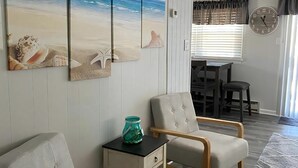 A room with a beach-themed wall art, two upholstered chairs, a small table with a glass jar, and a rug. - Newly renovated duplex located on the ocean block in the heart of Surf City. (Surf City)