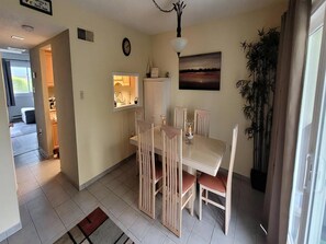 A dining area with a table and chairs, a clock, a painting, and a potted plant. - Ship Bottom Ocean Block with Pool (Ship Bottom)