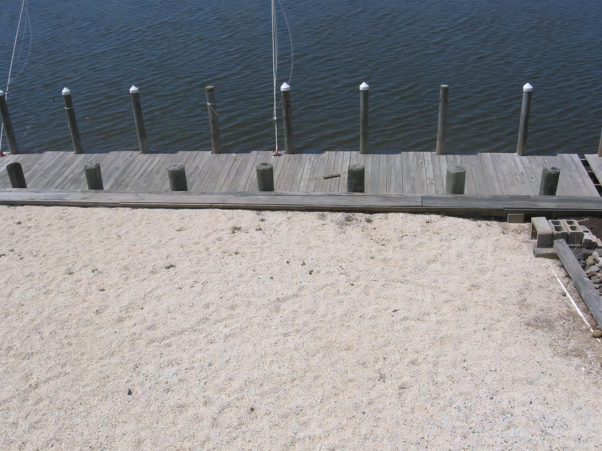Een houten pier die zich uitstrekt over kalm water, met een zandstrand op de voorgrond.