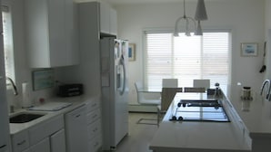 Una cocina moderna con armarios blancos, una isla central y una zona de comedor con mesa y sillas.