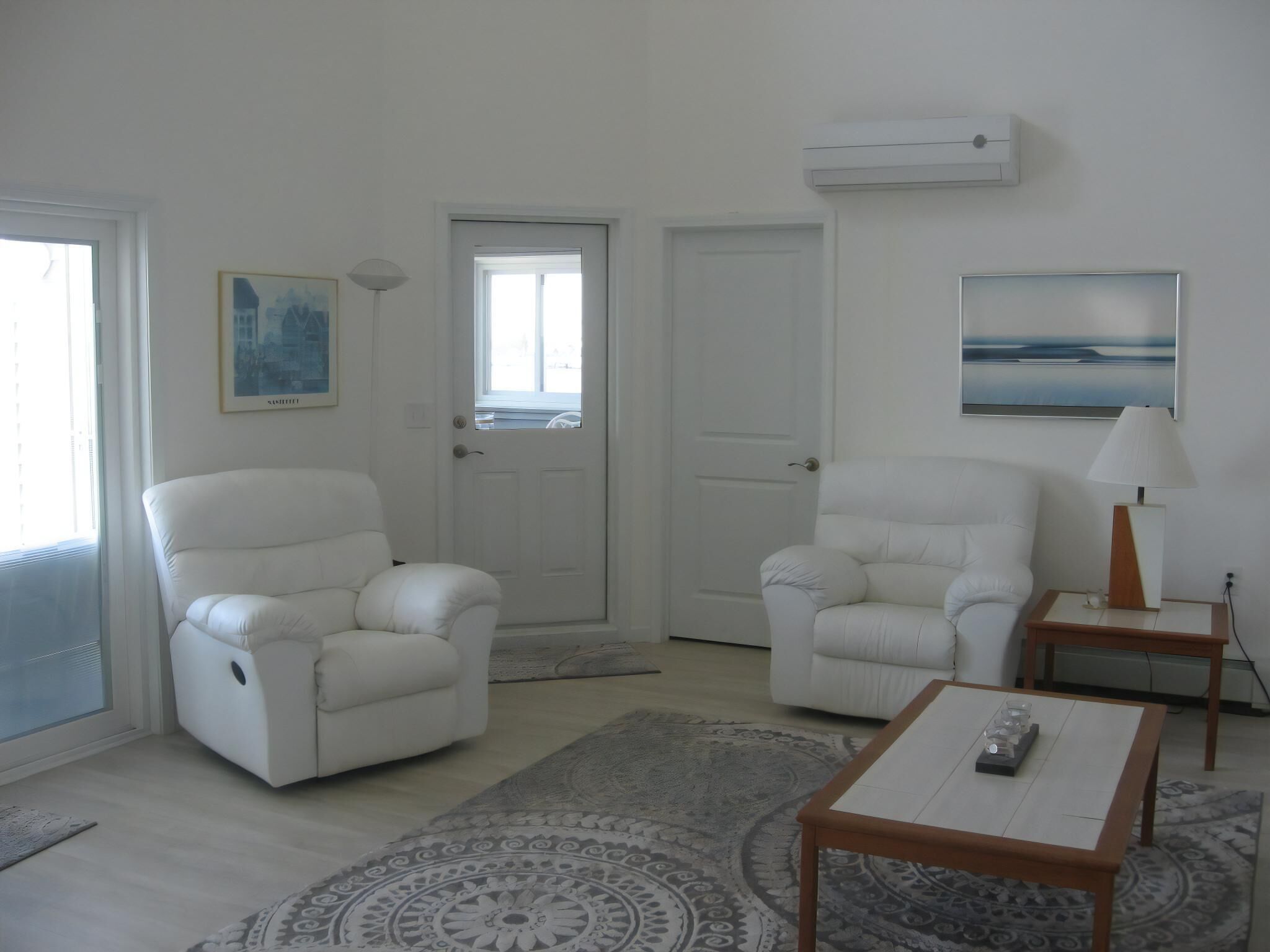 Un salon avec deux fauteuils blancs, une table basse, un tapis et un tableau accroché au mur.