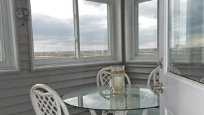 Una mesa con cubierta de vidrio, sillas, una puerta y vista a la playa a través de amplias ventanas.