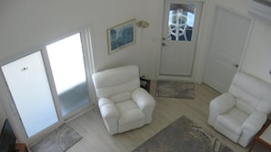 Una sala de estar con dos sillones blancos, un tapete estampado y una puerta con panel de vidrio.