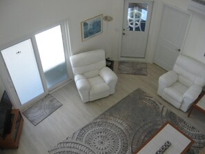 A living room with two white armchairs, a patterned rug, and a door with a glass panel.
