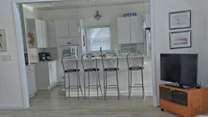 Una sala de estar moderna con televisor de pantalla plana, un tapete estampado y un comedor con sillas de metal.