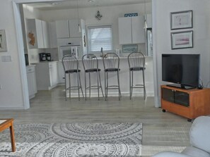 A modern living room with a flat-screen TV, a patterned rug, and a dining area with metal chairs.