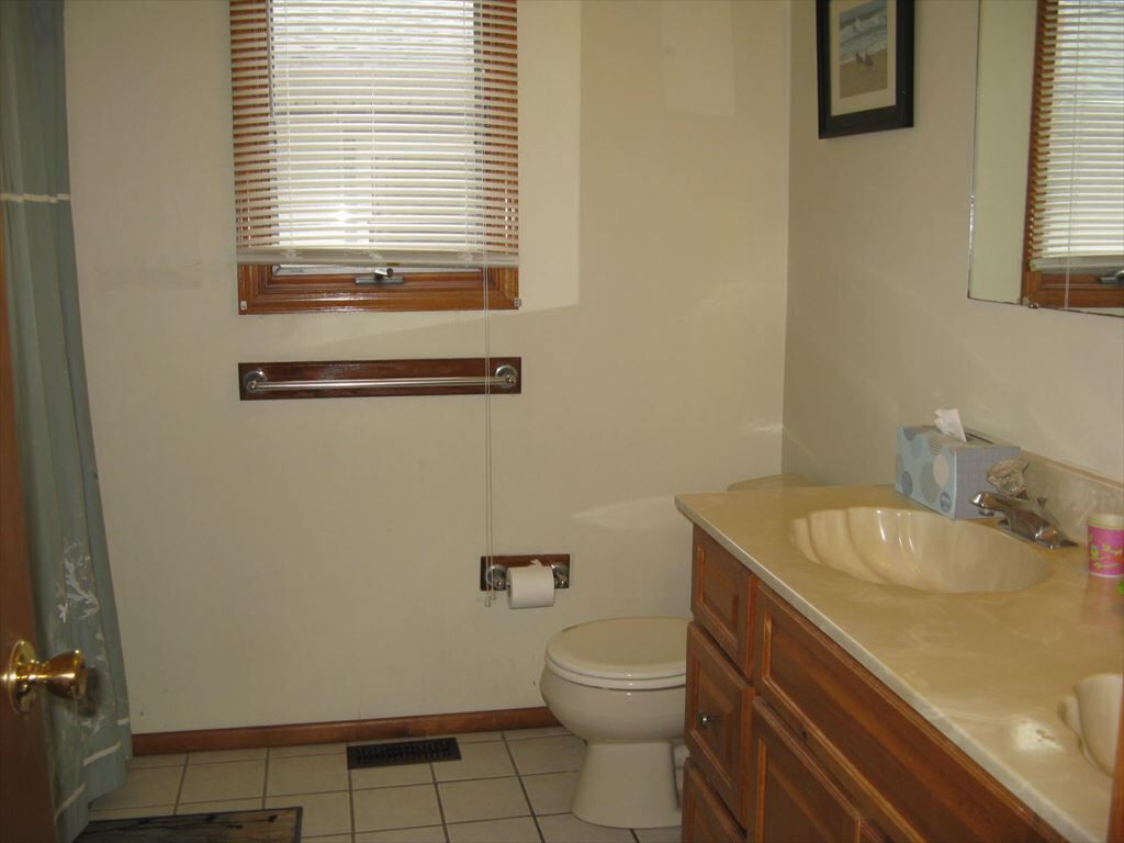 A bathroom with a toilet, sink, vanity, and window blinds.