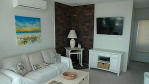 A living room with a white sofa, a white coffee table, a TV, and a brick wall.